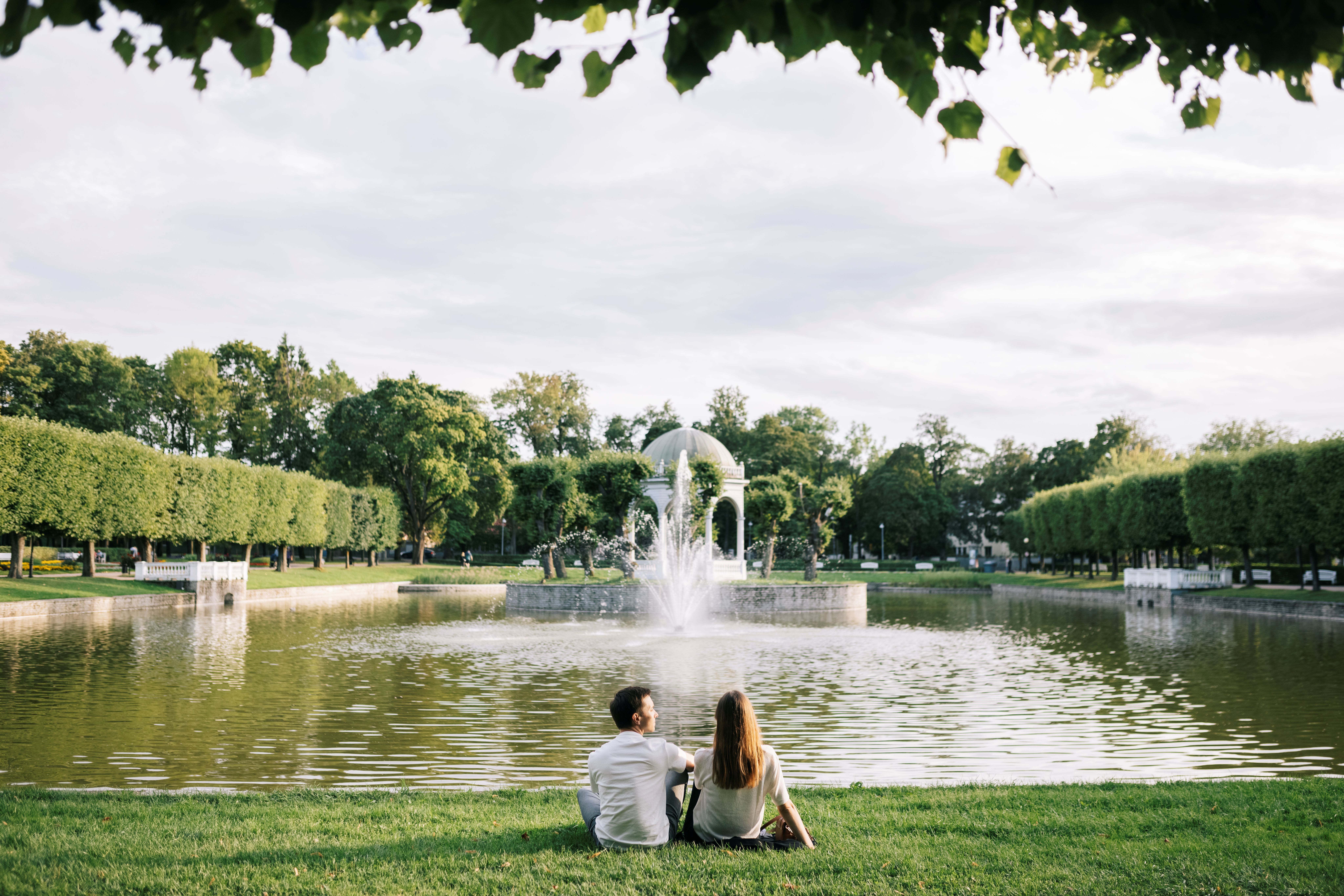 Мужчина и женщина сидят на траве у лебединого пруда и павильона в парке Кадриорг