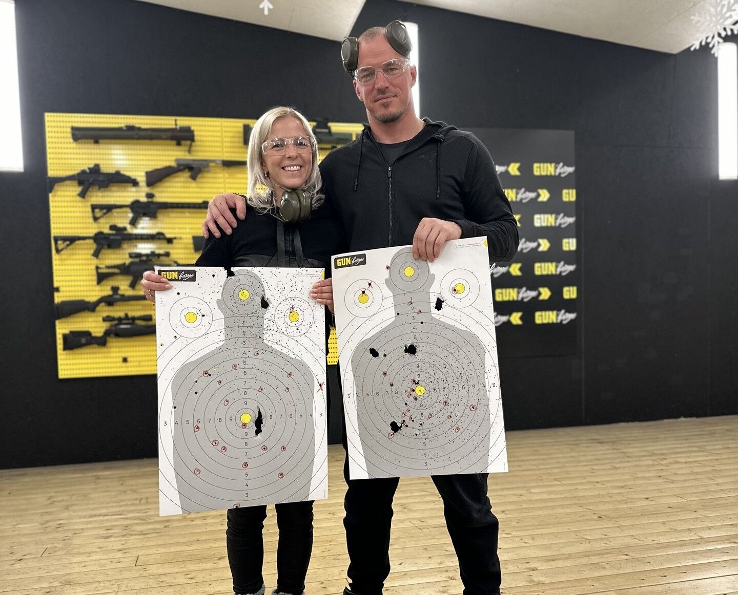 Tallinnas Pirital Gun Garage lasketiirus poseerivad kaks inimest naeratades koos oma m&auml;rklehtedega. M&otilde;lemal on k&auml;es paberist sihtm&auml;rgid, millele on lastud k&uuml;mneid laske, osa tabamustest otse keskele. Taustal paistab kollane relvasein, kus reas erinevad p&uuml;ssid.