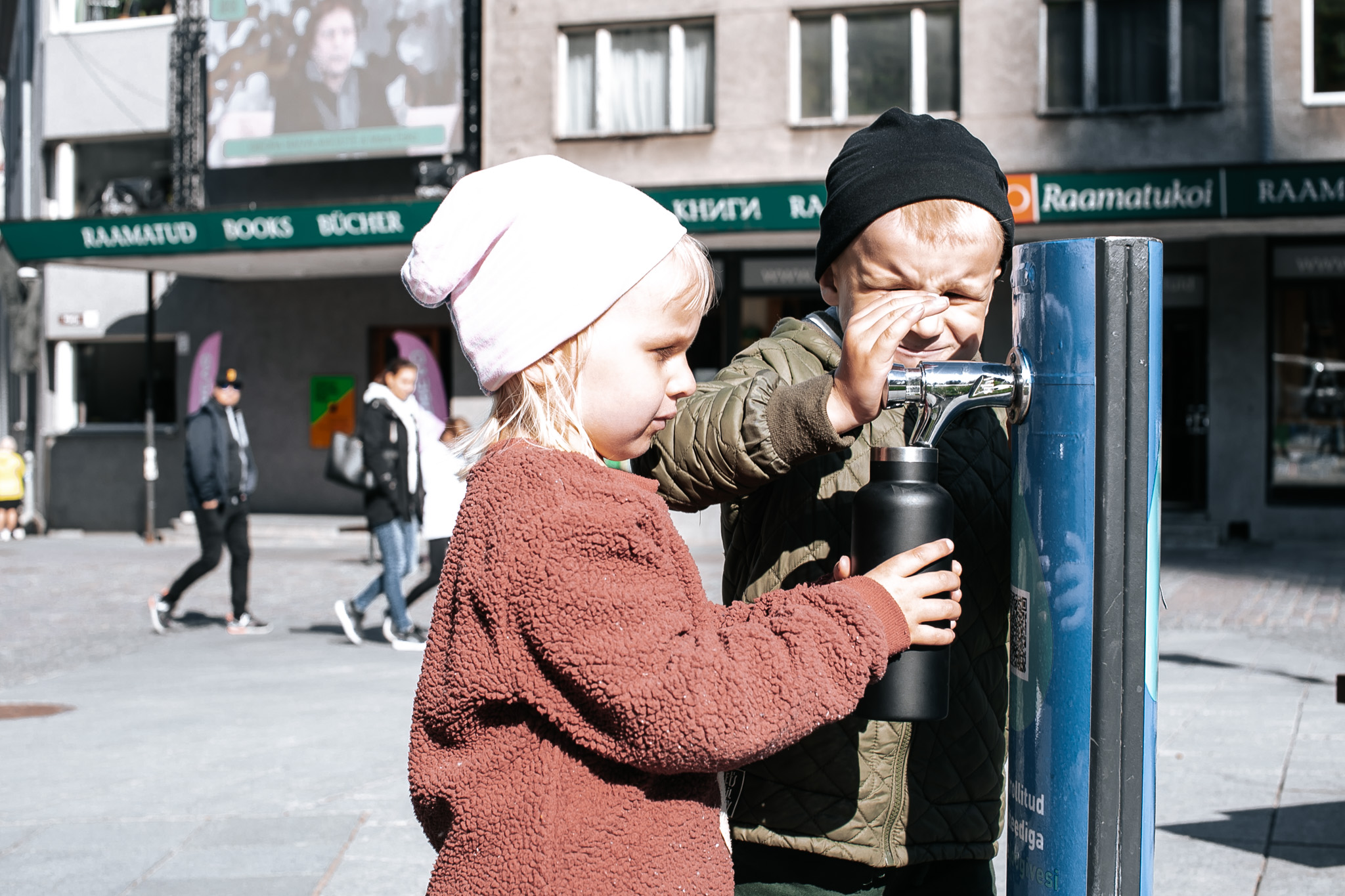 Kaksi lasta ottamassa puhdasta juomavettä hanasta Tallinnan vanhassakaupungissa
