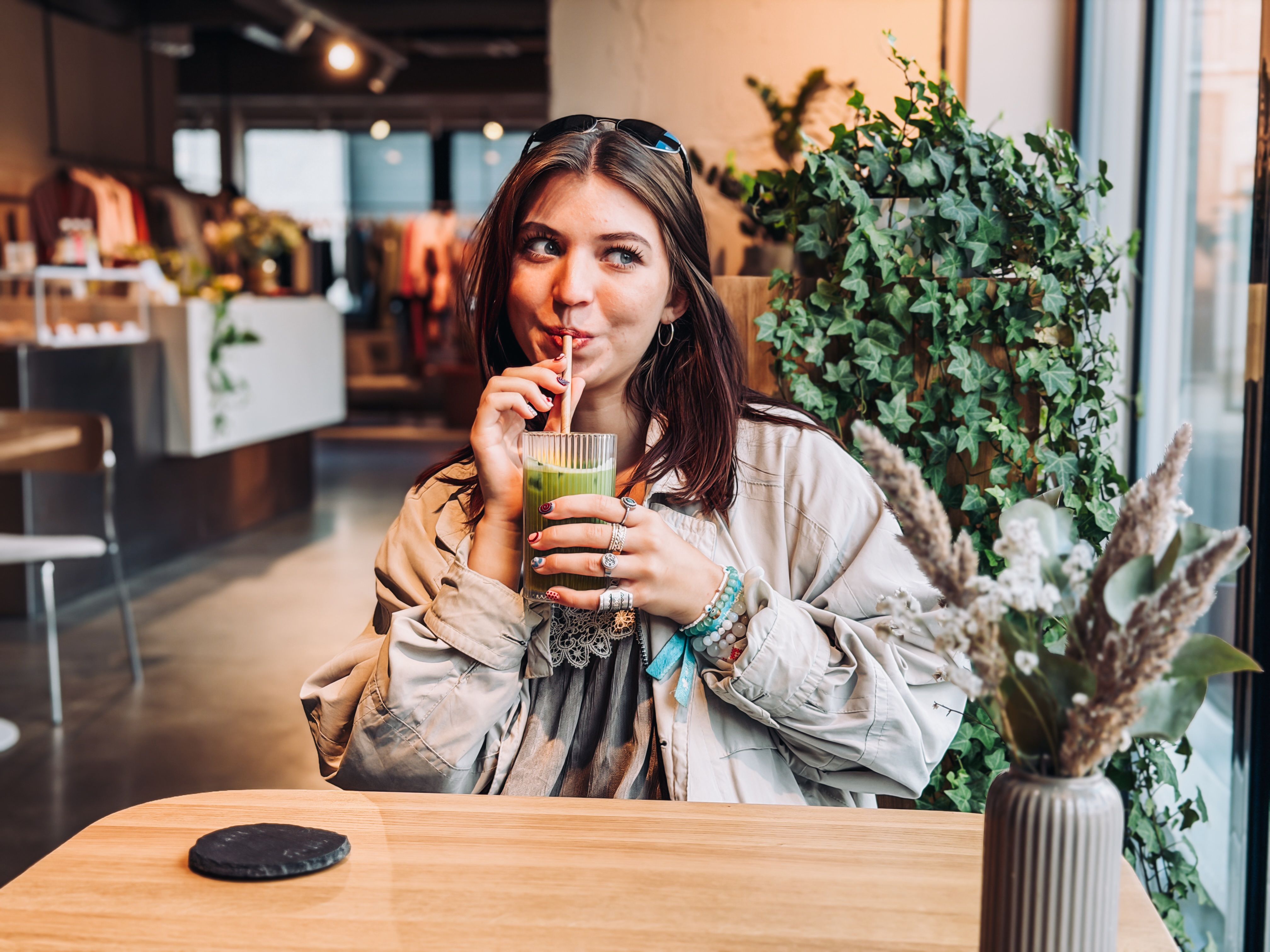 Getter drinks green matcha in a bright caf&eacute; in North Tallinn, seated by a window with leafy plants and a vase on the table.