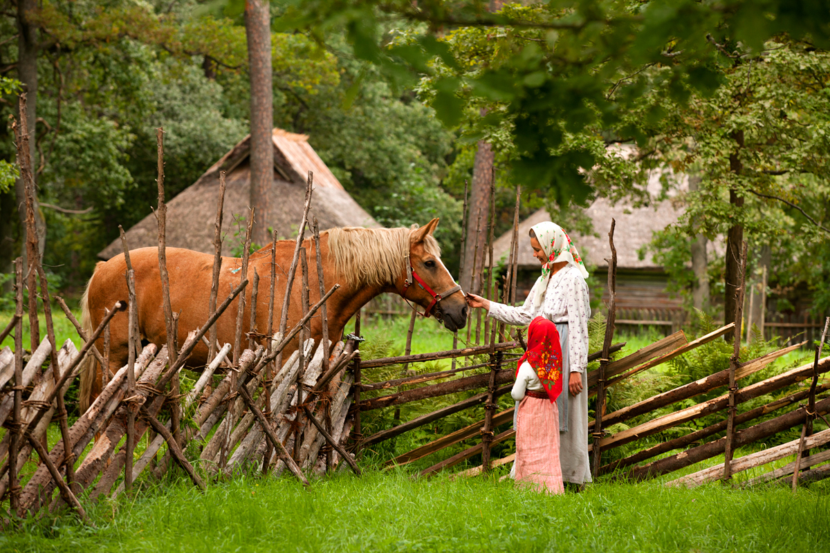 Roigasaia ääres seisev talunaine silitab hobuse nina Eesti Vabaõhumuusemis Tallinnas