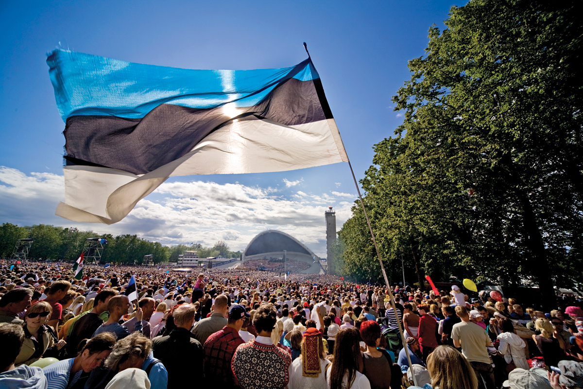 rahvast täis Tallinna lauluväljak laulupeo ajal, esiplaanil suur Eesti lipp