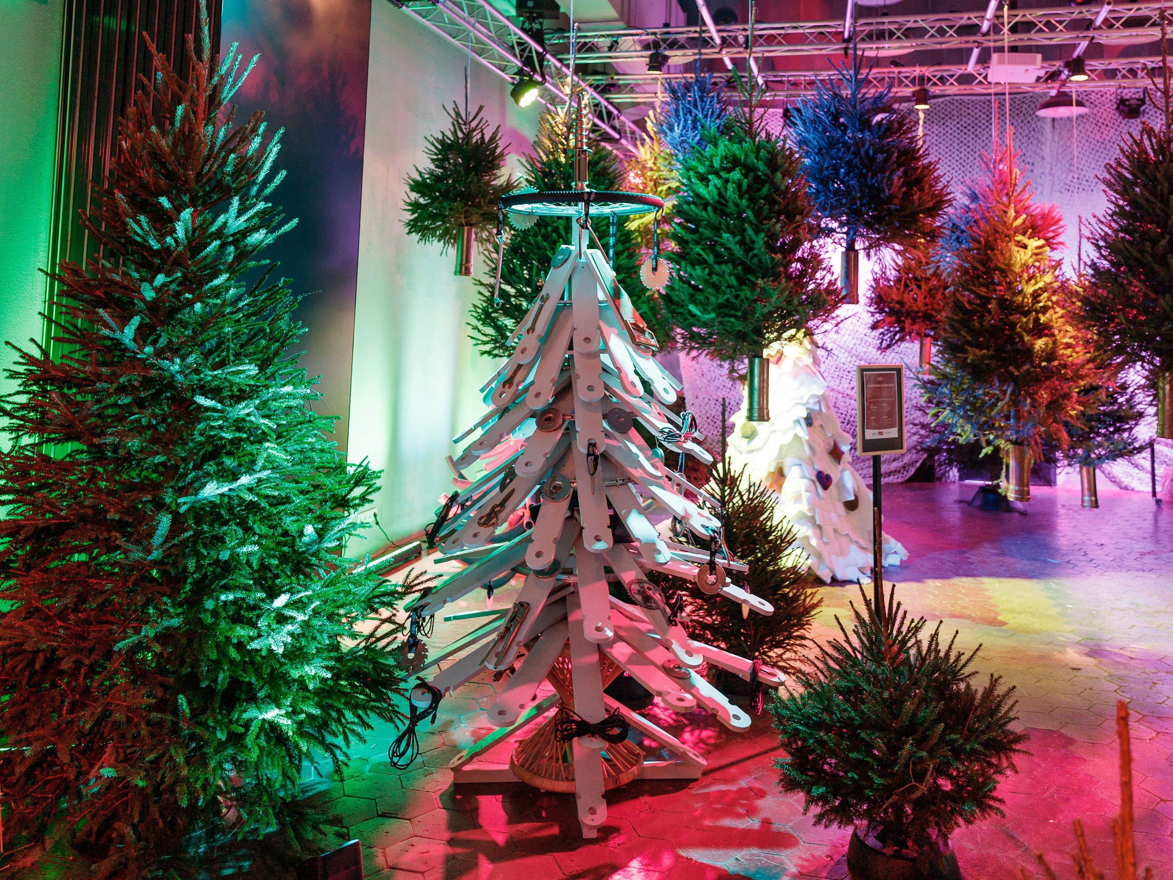 Värviliselt valgustatud jõulupuud Tallinna PROTO Avastustehases, keskel valge kunstpuu, mille taga on üles riputatud kuused futuristlikus ruumis.