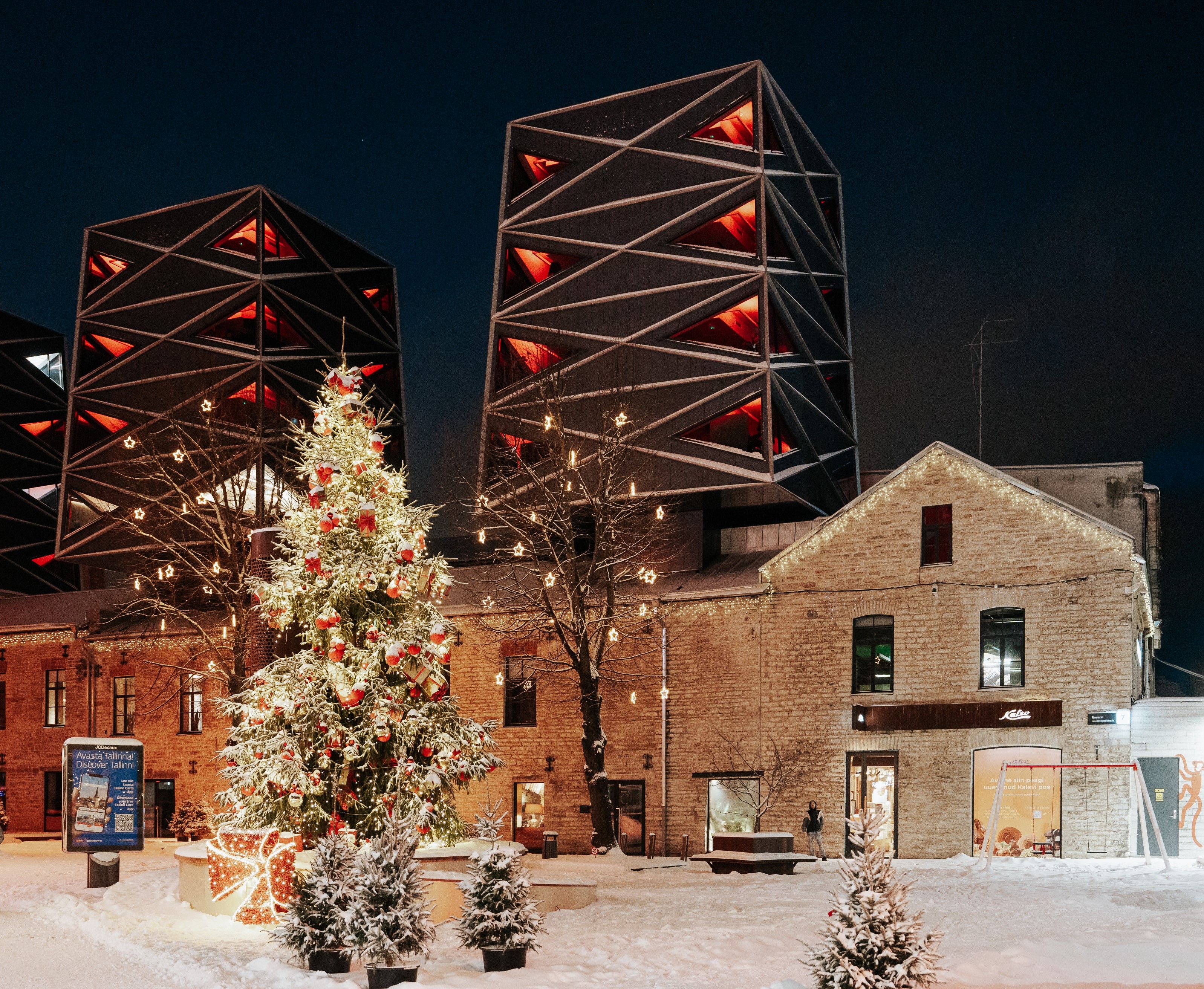 Lumine jõulupuu Tallinna Rotermanni kvartalis moodsate geomeetriliste hoonete ees, kaunistatud valgete ja punaste ehete ning säravate tuledega.