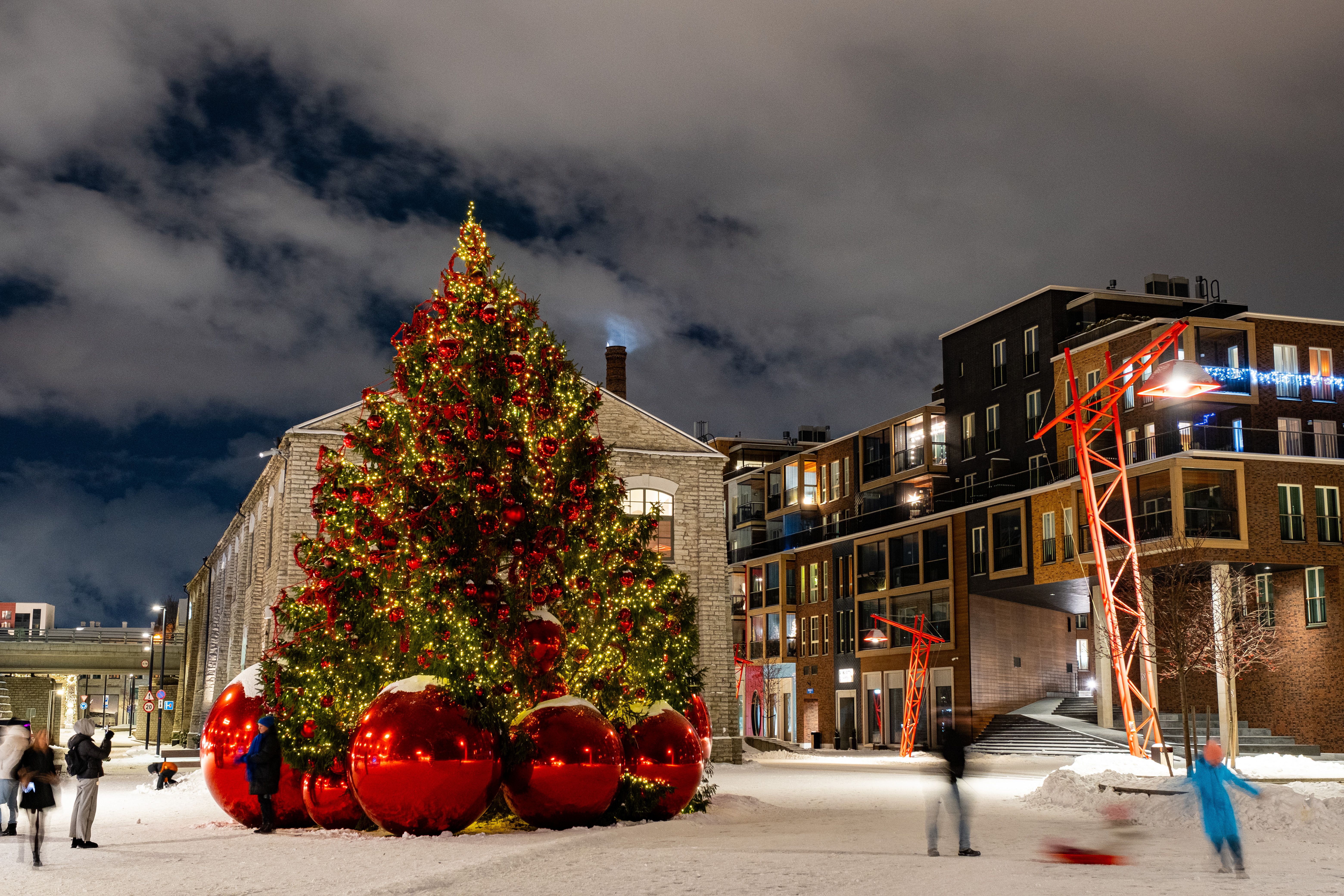 Suur jõulupuu Noblessneri väljakul Tallinnas, ümbritsetud hiiglaslike punaste jõulukaunistustega ning kaasaegsete hoonetega lumisel talveõhtul.