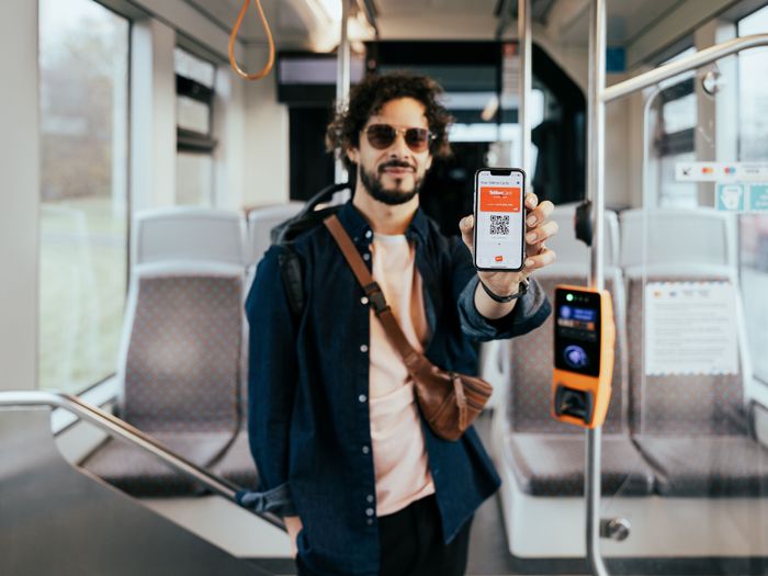 Man standing in public transport holding a mobile phone that displays the Tallinn Card app.