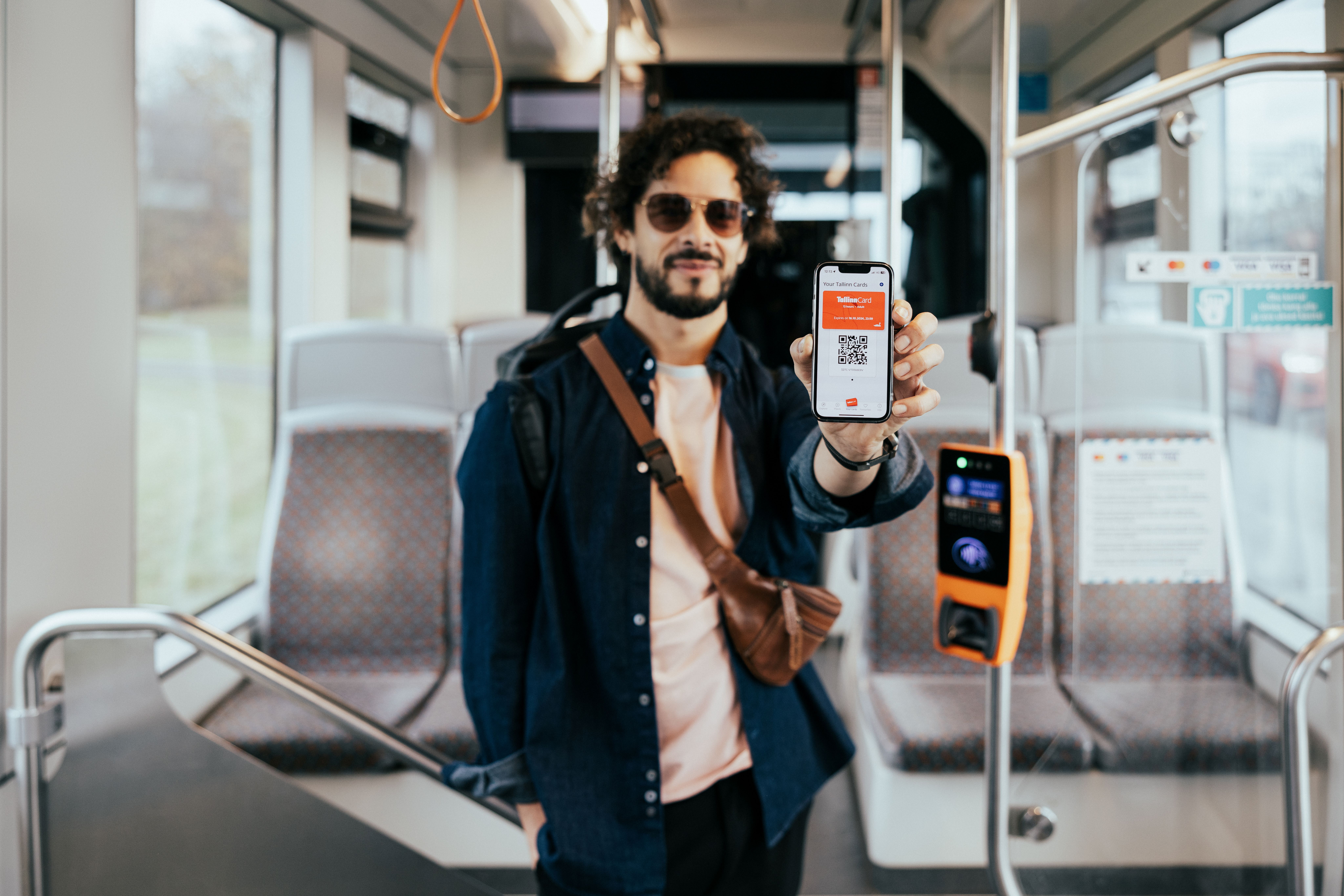 P&auml;ikseprillidega mees Tallinna &uuml;histranspordis hoiab mobiili, milles on avatud Tallinn Cardi mobiili&auml;pp.