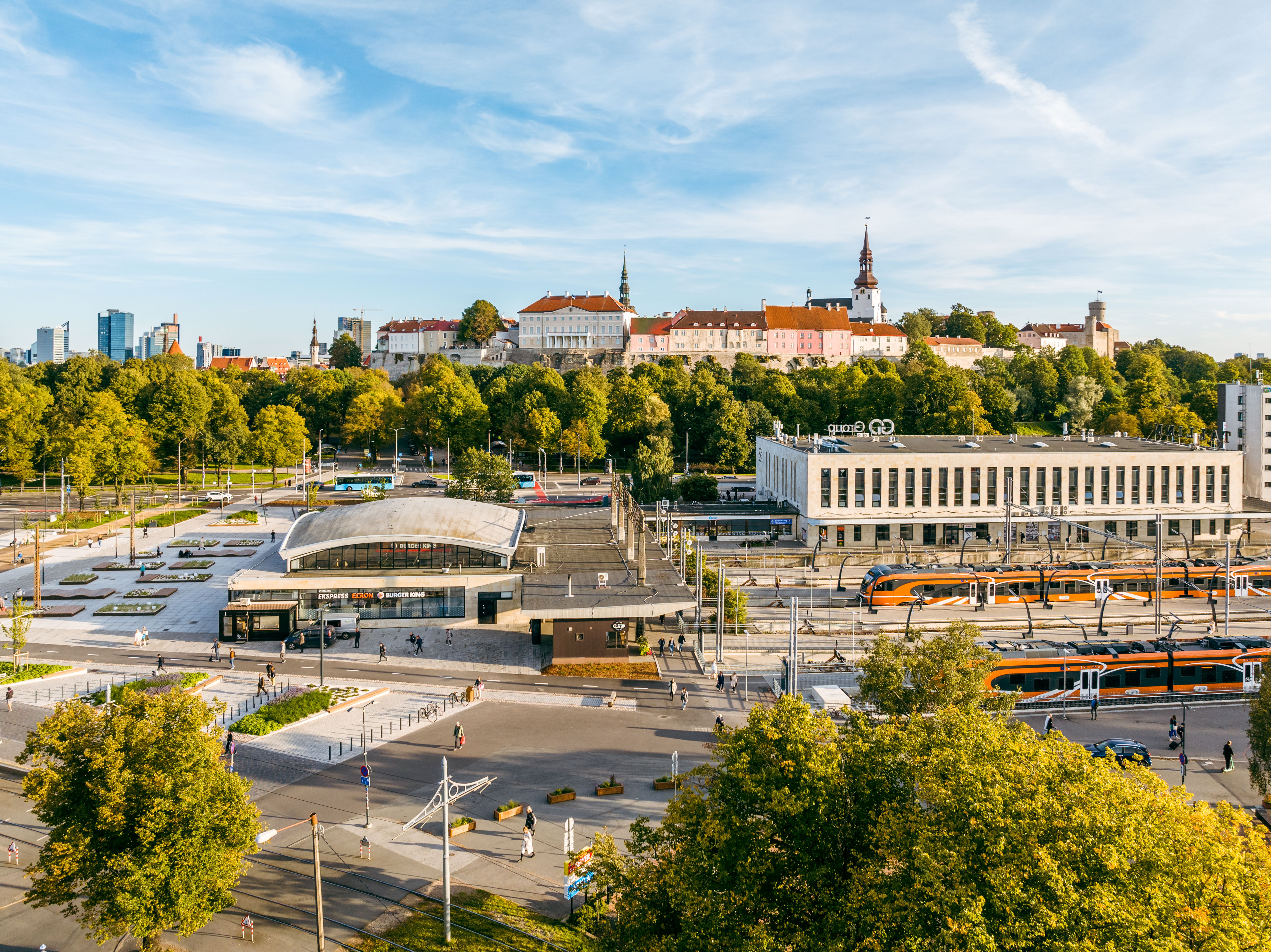 Aerial view of Tallinn's Balti Jaam train station with trains by the platforms, station buildings and a view of the Old Town in the background.