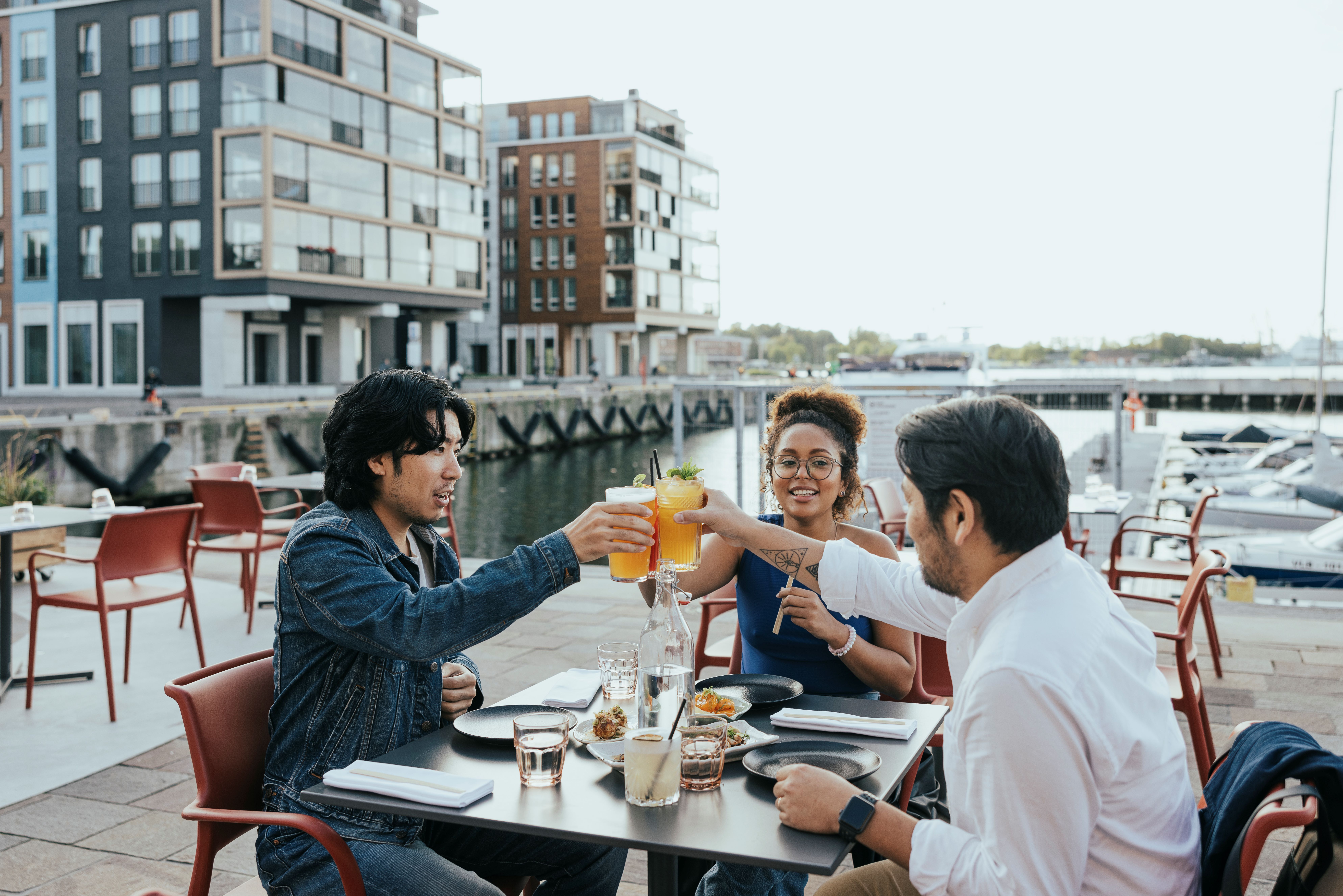 Three friends sitting and toasting at a restaurant table in the Noblessner seafront area of Tallinn, Estonia.