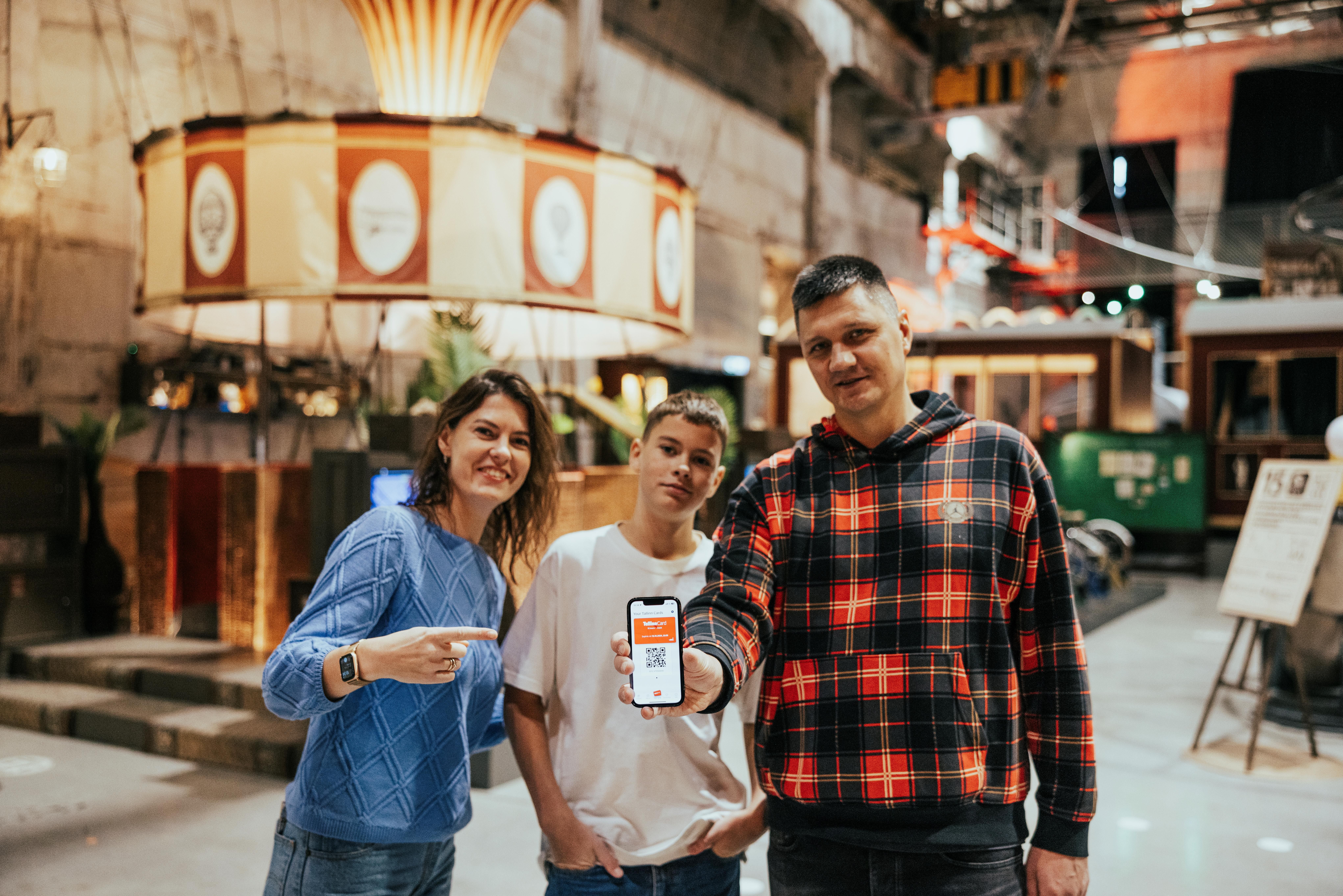 A family of three in the Proto Invention Factory in the Noblessner district in Tallinn; the mother pointing at the Tallinn Card app on her phone.