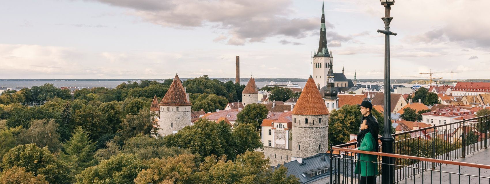 People admire Tallinn Old Town from Patkuli viewing platform, with St. Olaf’s Church and medieval towers in the background.
