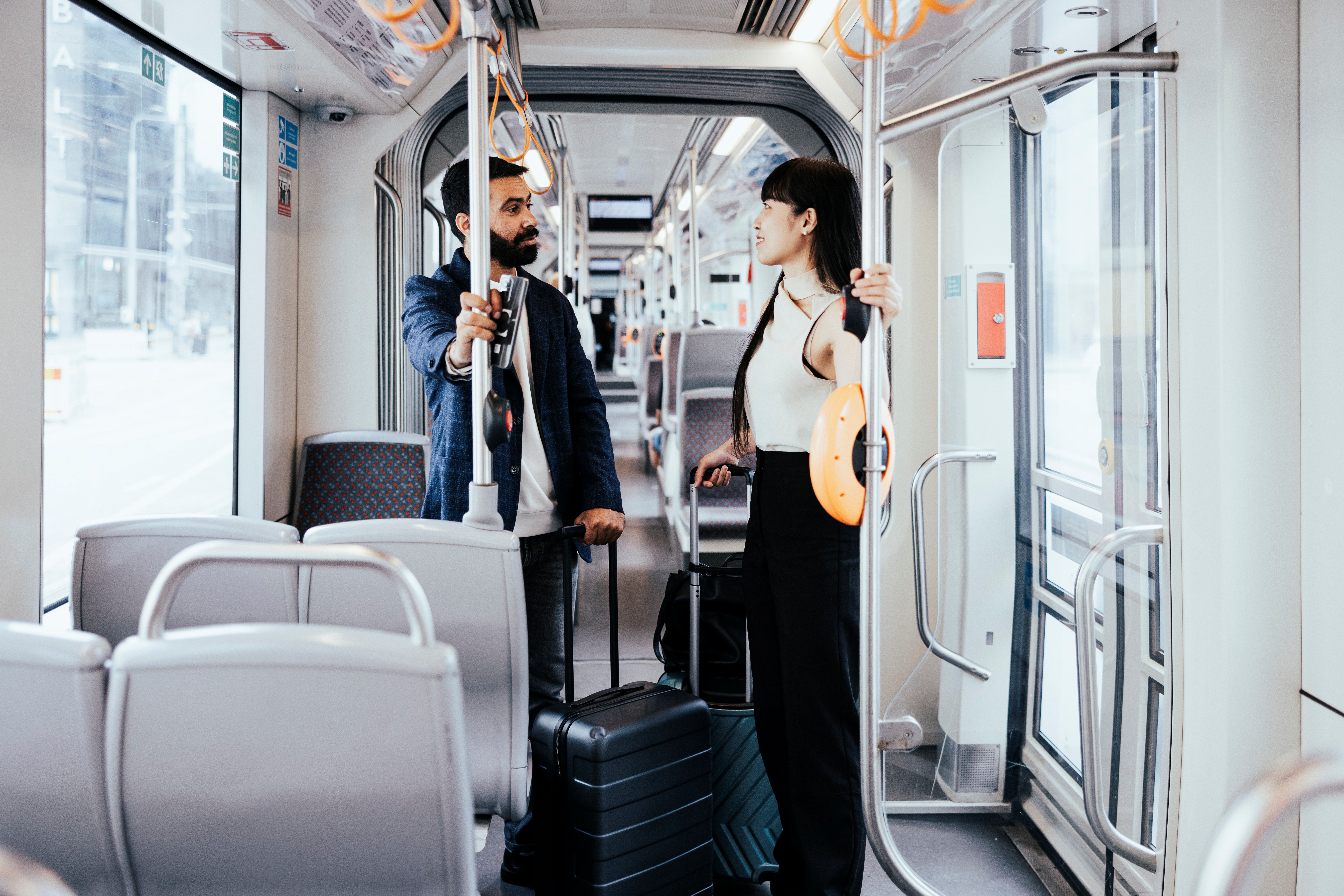 Two passengers with suitcases talking inside a modern Tallinn tram during a public transport journey.